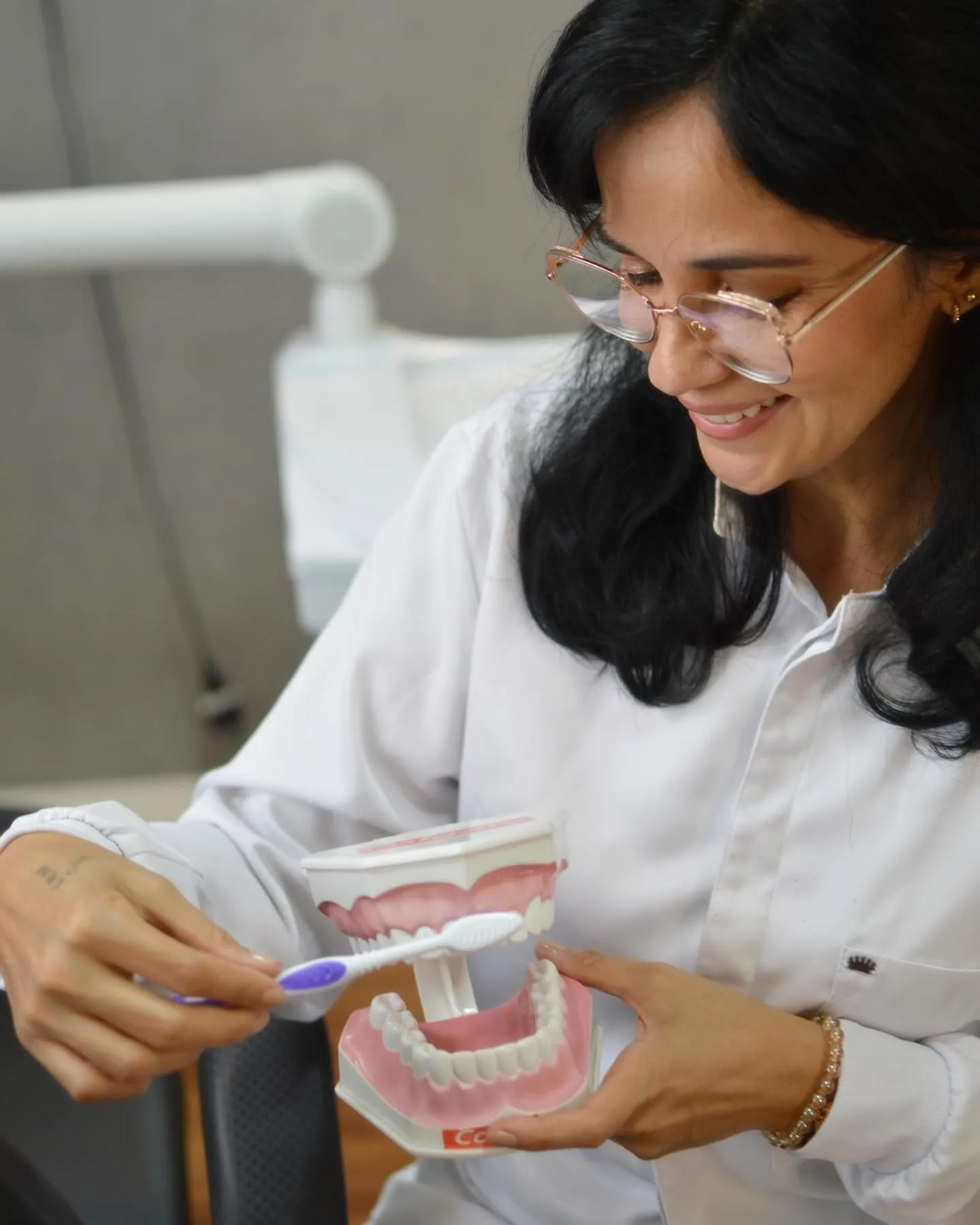 Dra. Judy Arrais segurando modelo didático de dentes e escova, sorrindo no consultório