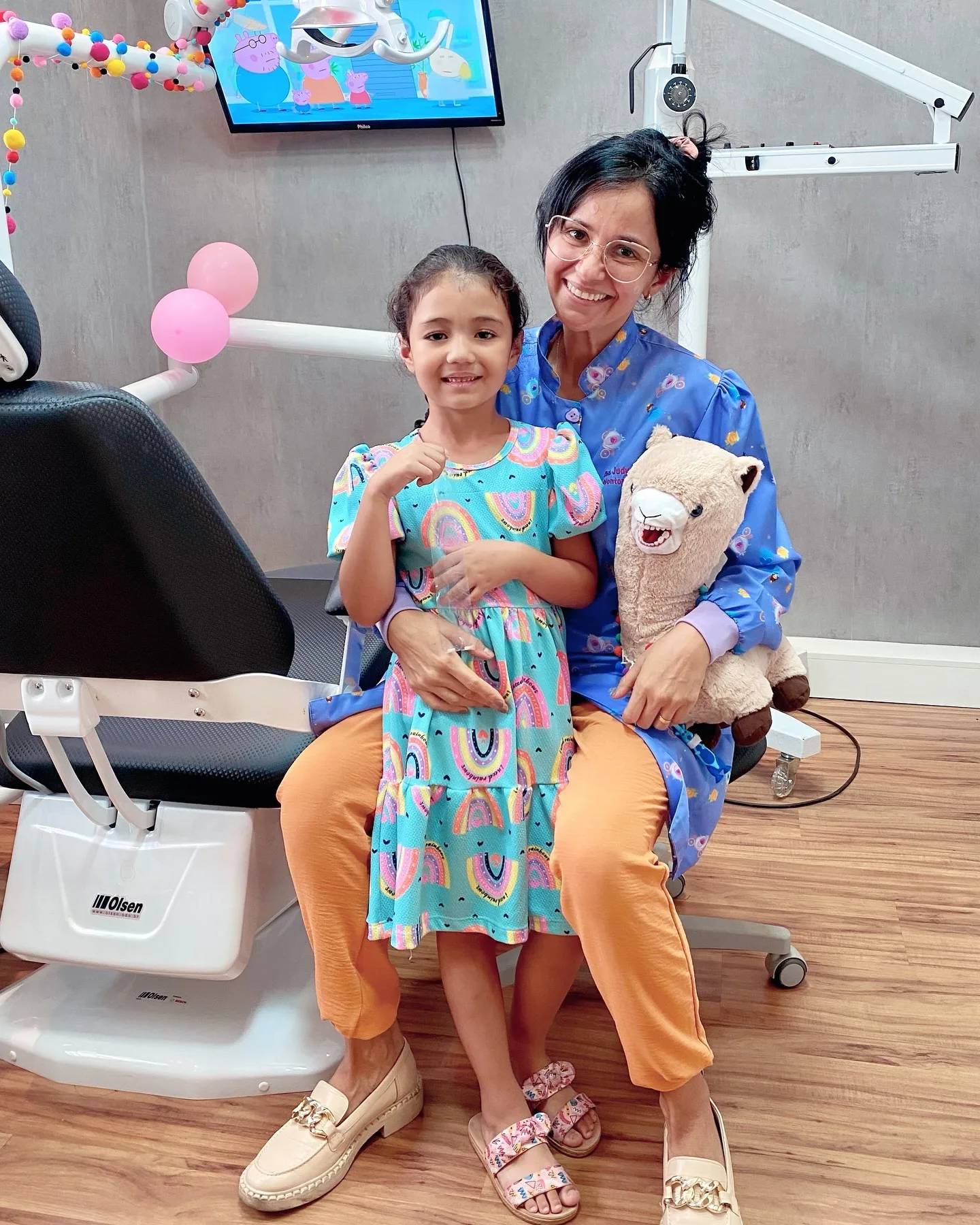 Dra. Judy Arrais com paciente pediátrica e ursinho no consultório